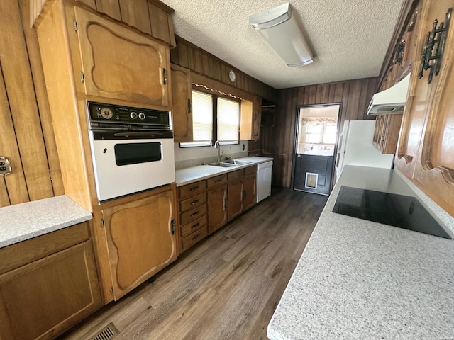 kitchen with white appliances, wooden walls, light countertops, and a sink