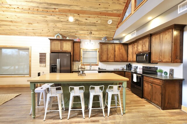 kitchen featuring a breakfast bar, visible vents, black range with electric stovetop, a kitchen island, and stainless steel fridge