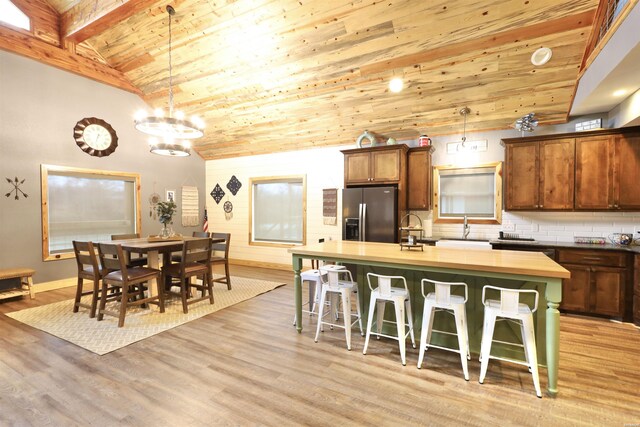 kitchen with wooden ceiling, a kitchen island with sink, hanging light fixtures, and stainless steel refrigerator with ice dispenser