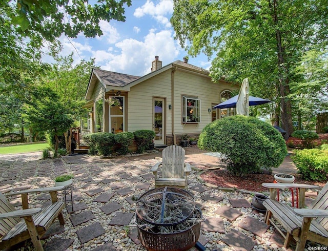 back of house featuring a shingled roof, an outdoor fire pit, a patio area, and a chimney