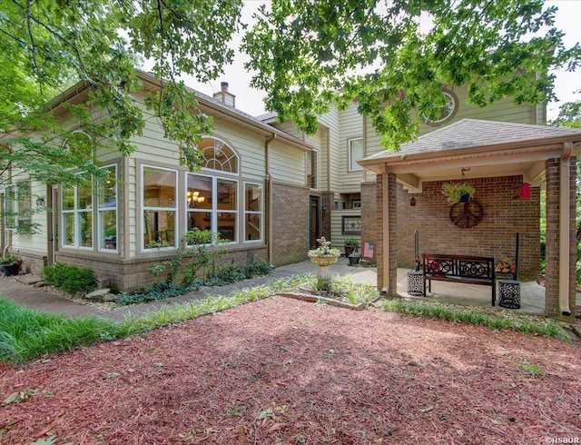 back of house featuring brick siding, a shingled roof, and a patio