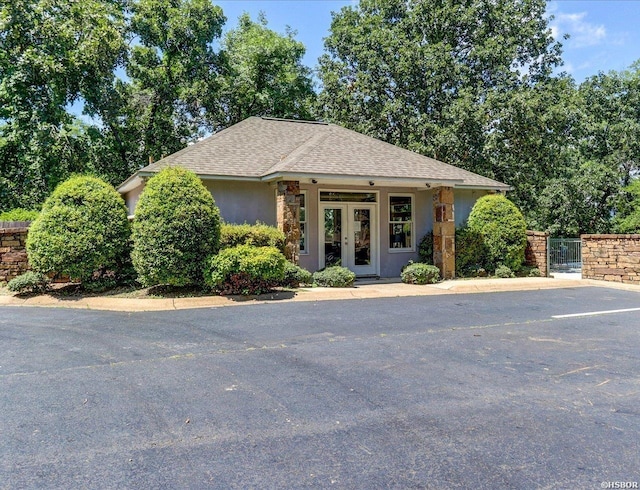 view of front of house with french doors, roof with shingles, fence, and stucco siding