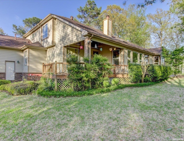 back of house featuring a chimney, a deck, and a lawn