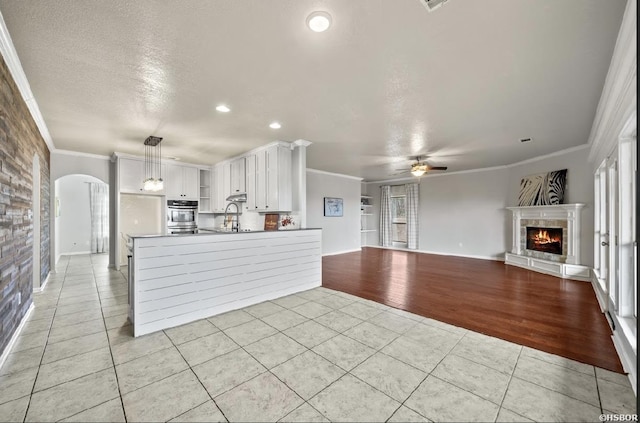 kitchen featuring light tile patterned floors, a ceiling fan, crown molding, and a tile fireplace