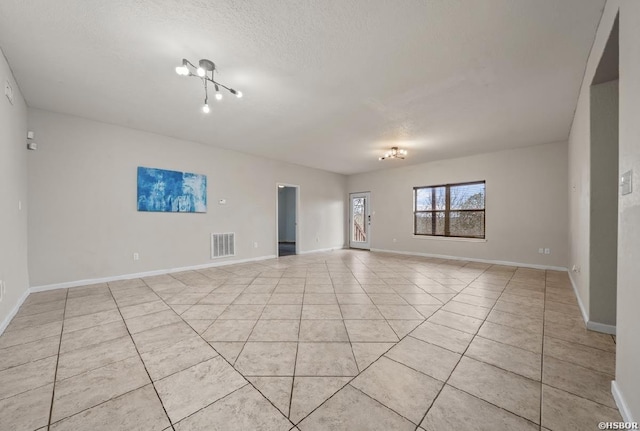 empty room with visible vents, baseboards, a chandelier, light tile patterned floors, and a textured ceiling