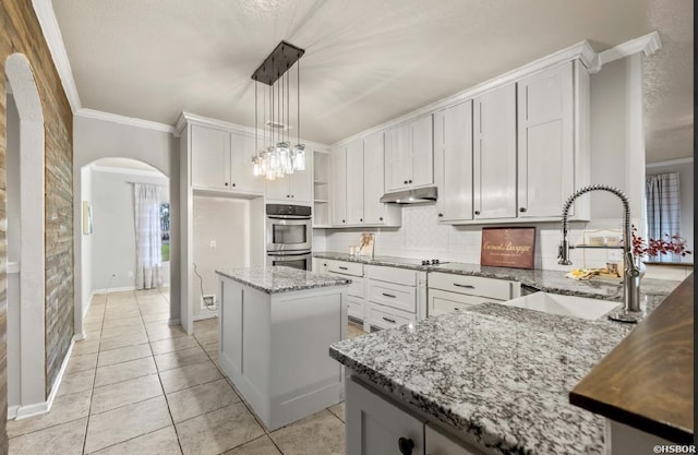 kitchen with open shelves, arched walkways, a sink, under cabinet range hood, and double oven