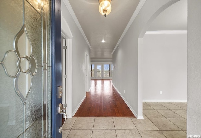 hallway featuring baseboards, arched walkways, crown molding, and tile patterned flooring