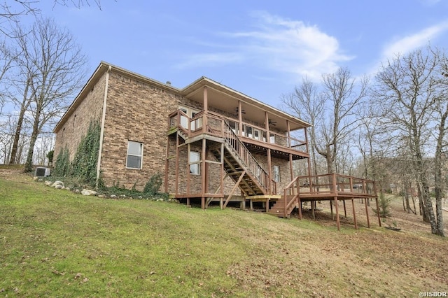 back of house with a ceiling fan, a wooden deck, stairs, a lawn, and brick siding