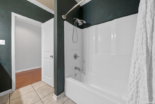 bathroom with tile patterned floors, a textured wall, baseboards, and shower / bath combo