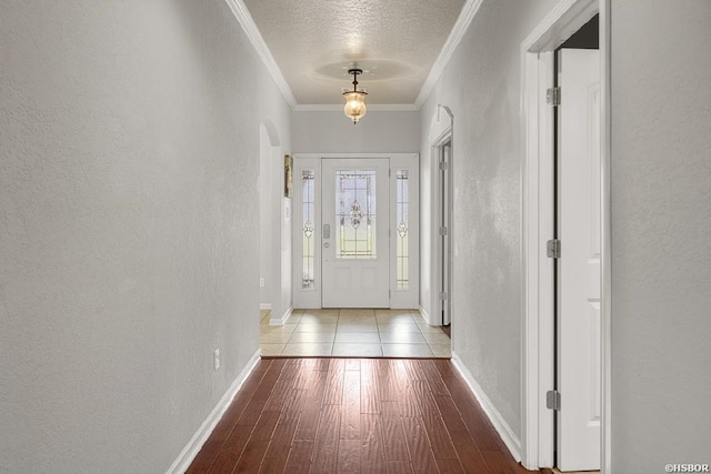 doorway featuring crown molding, a textured wall, wood finished floors, arched walkways, and a textured ceiling