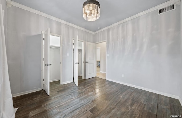 unfurnished bedroom with visible vents, ornamental molding, wood finished floors, an inviting chandelier, and baseboards