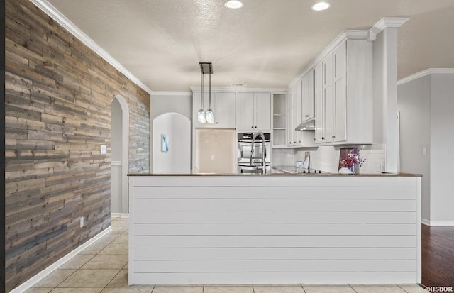 kitchen with ornamental molding, open shelves, arched walkways, a peninsula, and stainless steel oven