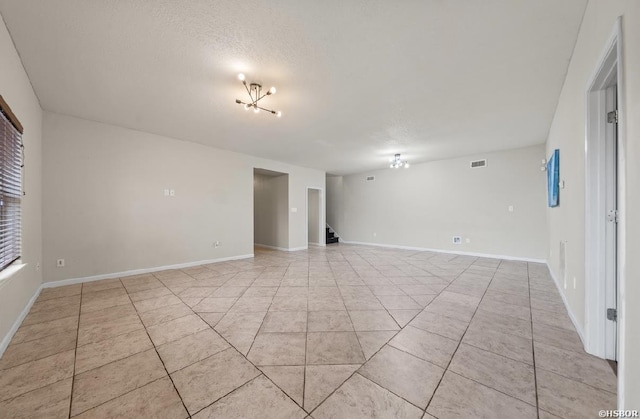 empty room with visible vents, a textured ceiling, an inviting chandelier, and light tile patterned flooring