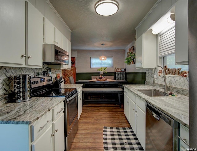 kitchen with white cabinets, appliances with stainless steel finishes, decorative light fixtures, crown molding, and a sink