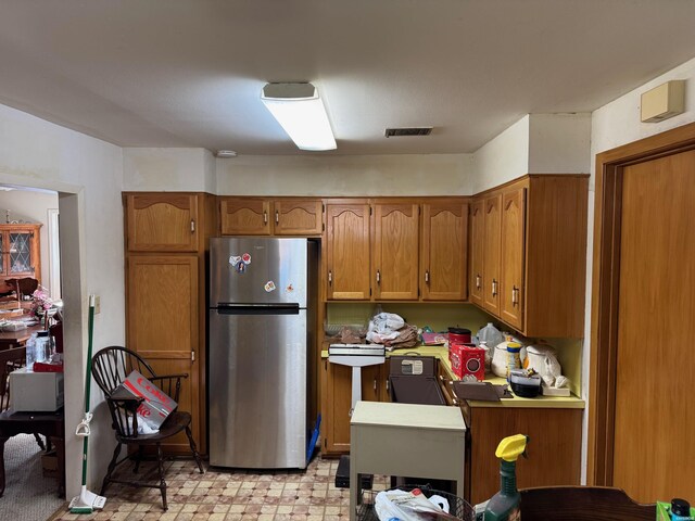 kitchen featuring light floors, visible vents, brown cabinets, and freestanding refrigerator