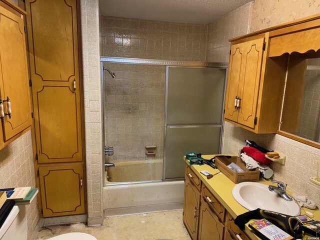 bathroom with tile walls, bath / shower combo with glass door, decorative backsplash, vanity, and a textured ceiling