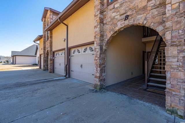 view of side of home with stone siding, stucco siding, driveway, and stairway