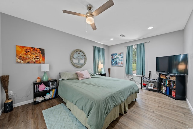 bedroom with a ceiling fan, visible vents, baseboards, and wood finished floors