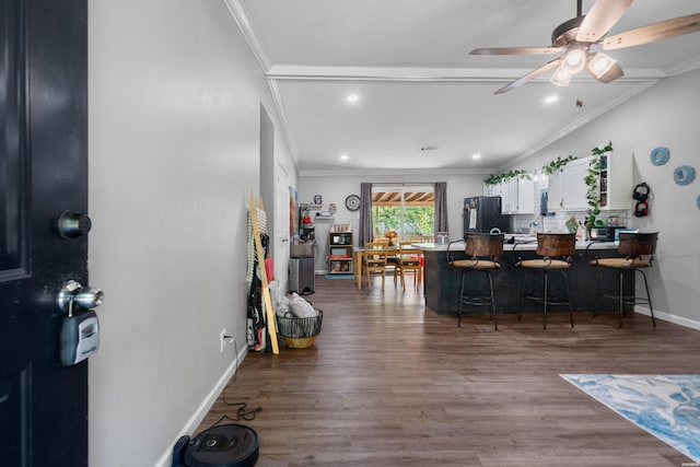 interior space featuring a breakfast bar area, ornamental molding, freestanding refrigerator, white cabinets, and wood finished floors