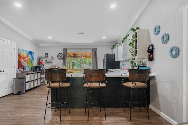 bar with visible vents, baseboards, light wood-type flooring, freestanding refrigerator, and crown molding