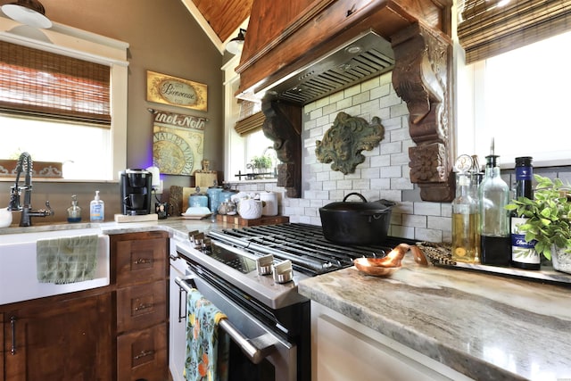 kitchen featuring stainless steel gas stove, a sink, light countertops, decorative backsplash, and custom exhaust hood