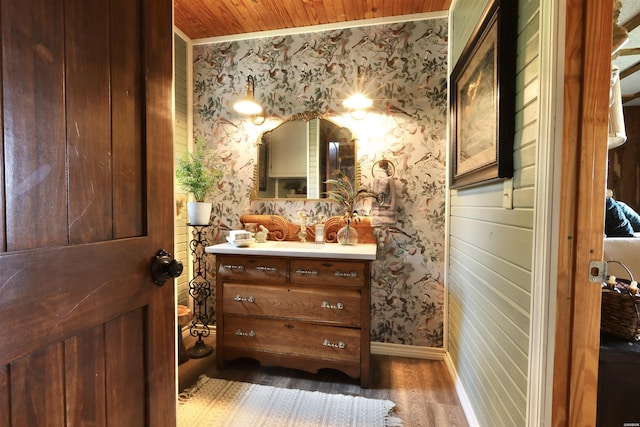 bathroom with wallpapered walls, vanity, baseboards, and wood finished floors