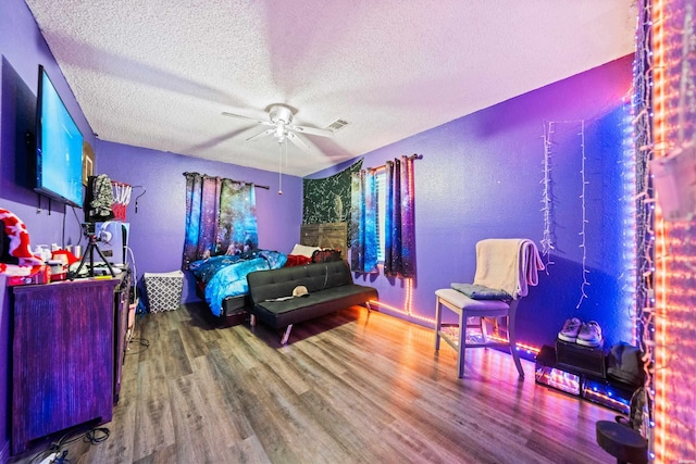 bedroom with a ceiling fan, a textured ceiling, visible vents, and wood finished floors