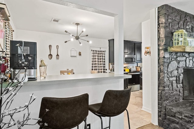 kitchen featuring a kitchen breakfast bar, light countertops, a notable chandelier, dark cabinetry, and stainless steel appliances