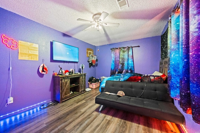 bedroom featuring visible vents, a textured wall, wood finished floors, ceiling fan, and a textured ceiling
