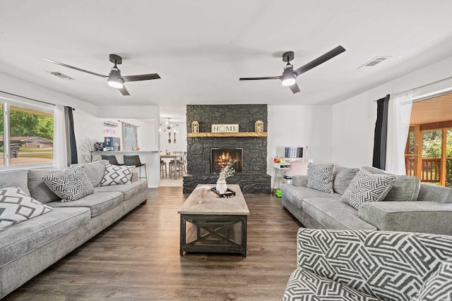 living room featuring visible vents, ceiling fan with notable chandelier, wood finished floors, and a stone fireplace