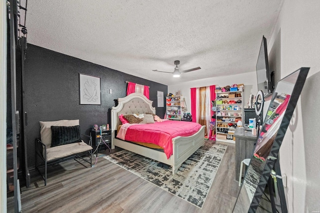 bedroom featuring a textured ceiling, ceiling fan, a textured wall, and wood finished floors