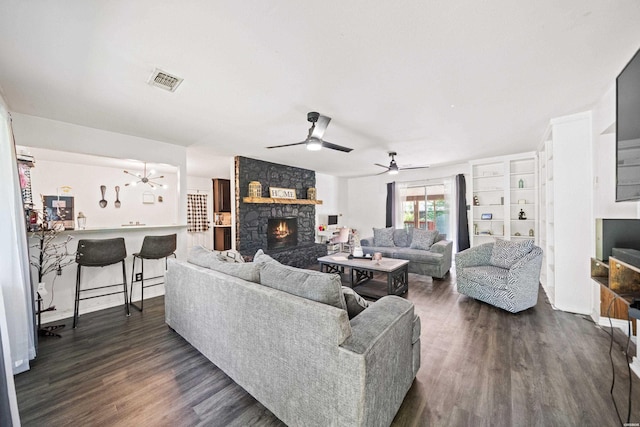 living area featuring ceiling fan, dark wood-style floors, a stone fireplace, and visible vents
