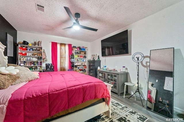 bedroom featuring visible vents, a textured ceiling, ceiling fan, and wood finished floors