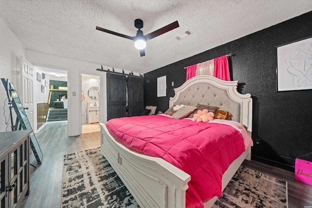 bedroom with visible vents, wood finished floors, a barn door, a textured ceiling, and a ceiling fan