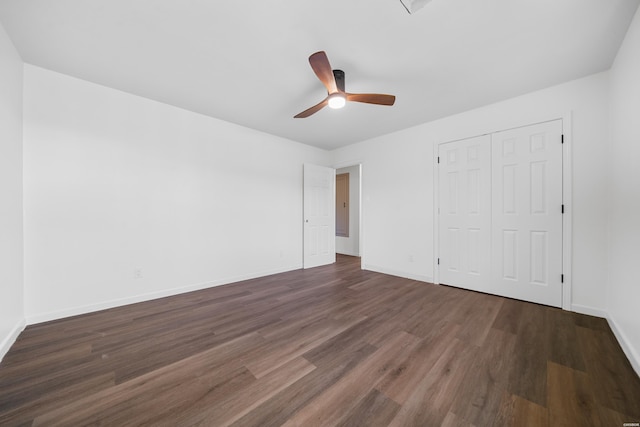 unfurnished bedroom featuring dark wood-type flooring, a closet, baseboards, and a ceiling fan