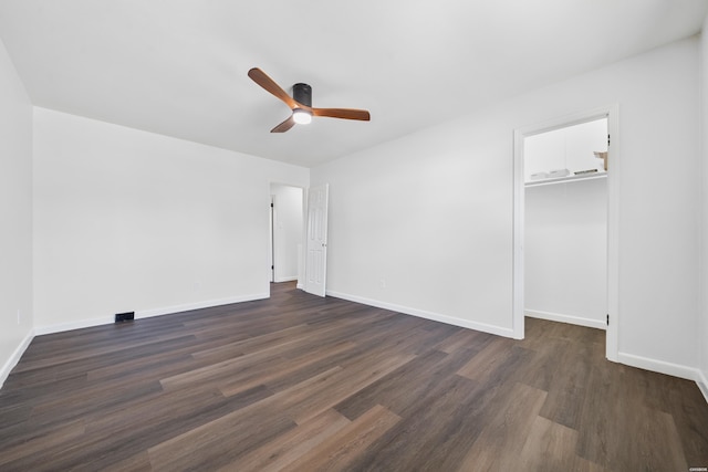 unfurnished bedroom featuring a walk in closet, a closet, dark wood finished floors, and baseboards