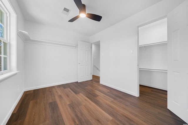 unfurnished bedroom with dark wood-style floors, multiple windows, visible vents, and baseboards