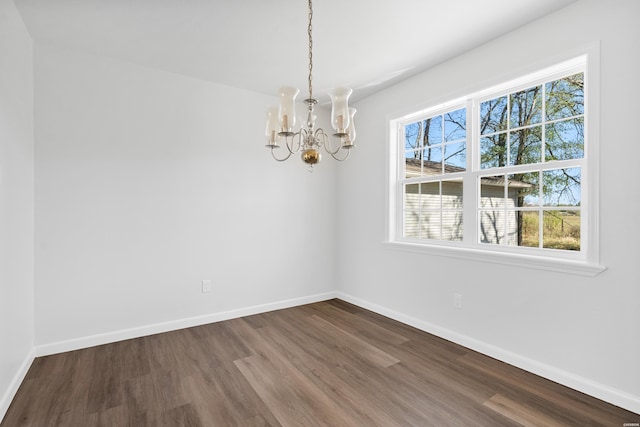 empty room with dark wood-style floors, a chandelier, and baseboards