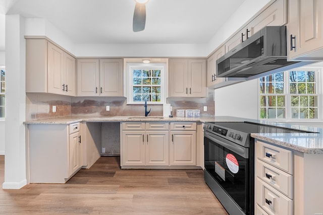 kitchen with decorative backsplash, appliances with stainless steel finishes, light stone counters, light wood-type flooring, and a sink