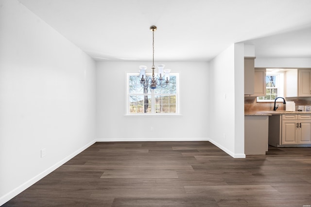 unfurnished dining area featuring a notable chandelier, baseboards, and dark wood-style flooring