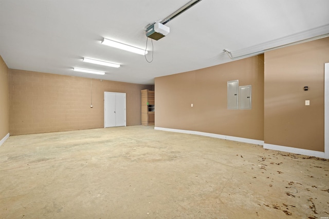 garage featuring a garage door opener, concrete block wall, electric panel, and baseboards