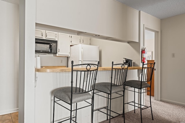 5371 Central Ave Unit 6G, Hot Springs, AR 71913 - kitchen featuring freestanding refrigerator, black microwave, a breakfast bar area, a textured ceiling, and white cabinetry