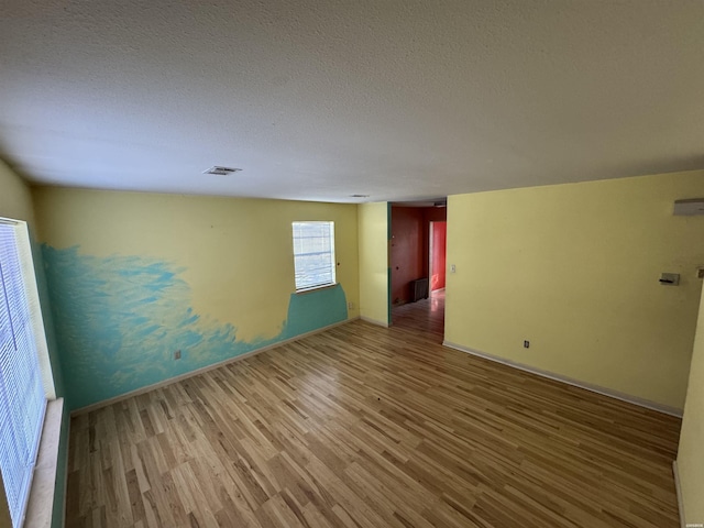 unfurnished room featuring baseboards, a textured ceiling, visible vents, and wood finished floors