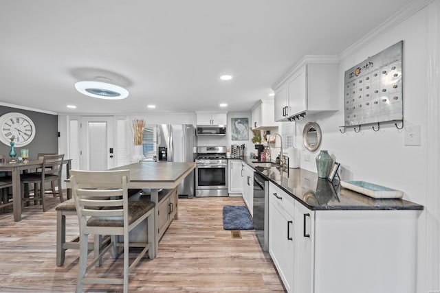 kitchen with ornamental molding, light wood-style floors, white cabinets, stainless steel appliances, and a sink