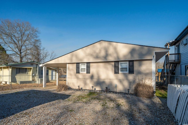 rear view of property featuring an attached carport, gravel driveway, and fence