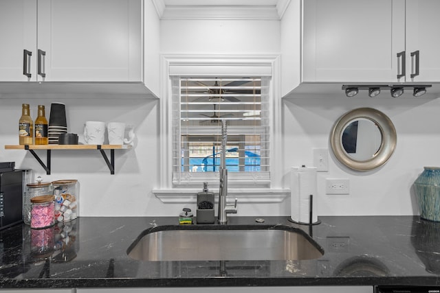 kitchen with dark stone countertops, white cabinets, crown molding, and a sink