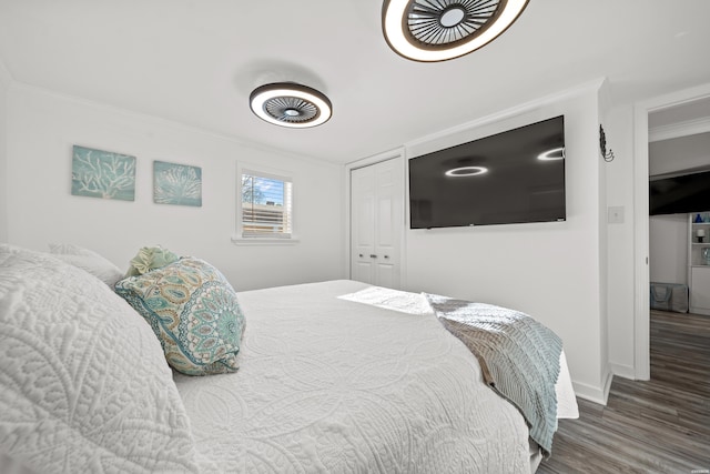 bedroom with a closet, baseboards, wood finished floors, and ornamental molding