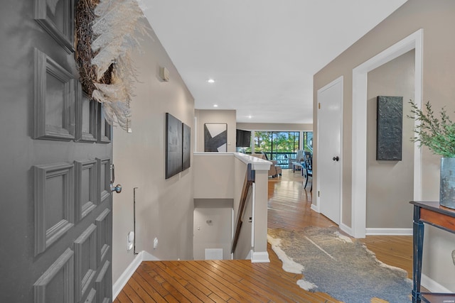 hallway with recessed lighting, wood finished floors, an upstairs landing, and baseboards