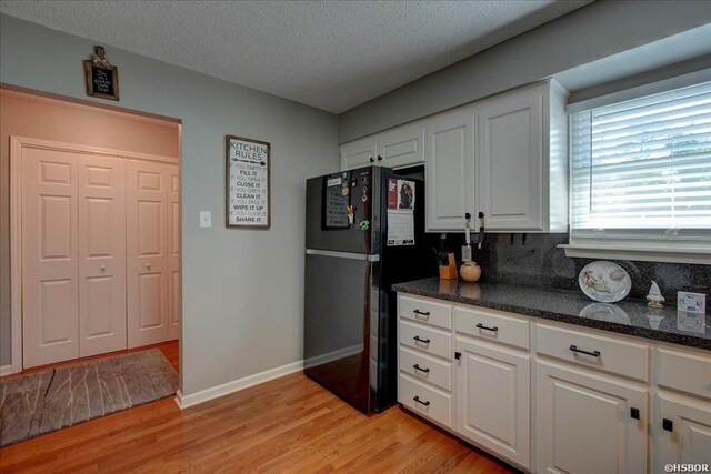 kitchen featuring baseboards, light wood-style flooring, freestanding refrigerator, a textured ceiling, and white cabinetry