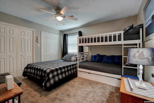 bedroom with carpet floors, a textured ceiling, a ceiling fan, and two closets